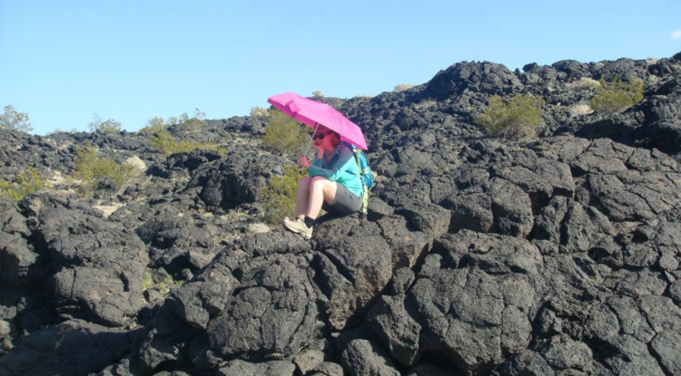 Ali Bramson sits on lava rocks holding pink umbrella