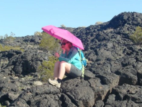 Ali Bramson sits on lava rocks holding pink umbrella