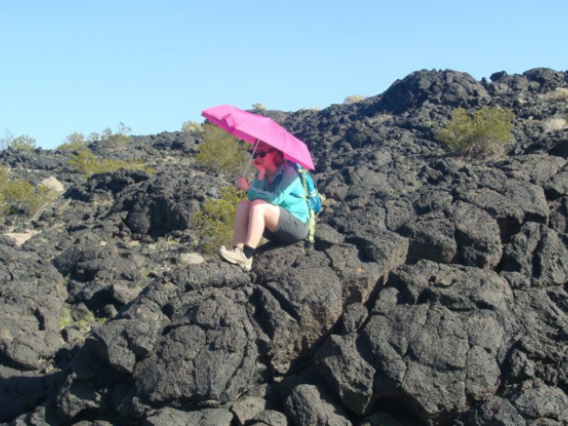 Ali Bramson sits on lava rocks holding pink umbrella