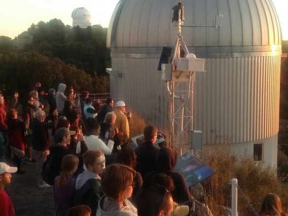 A large group of UA Space Grant Interns, SEDS and Astronomy Club members watch sunset at Kitt Peak Observatory, with telescopes in background.