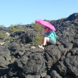 Ali Bramson sits on lava rocks holding pink umbrella
